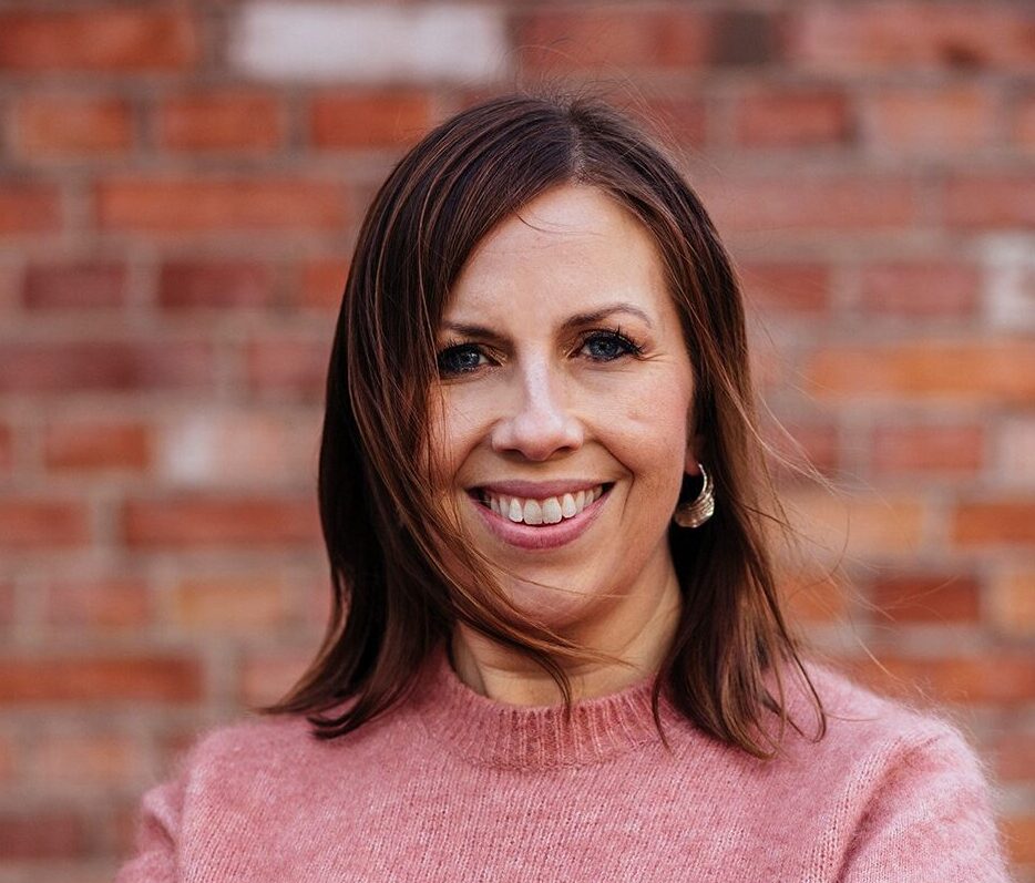 Maria stands in a knitted sweater and smiles into the camera.
